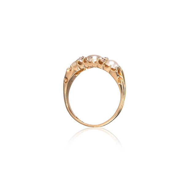 A gold ring featuring a cluster of white pearls at the top, shown against a plain white background with a soft reflection below.