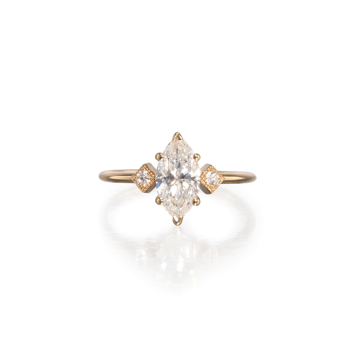 A yellow gold ring featuring a marquise-cut diamond center stone with two smaller round-cut diamonds on the sides, set against a clean white background with a soft reflection.