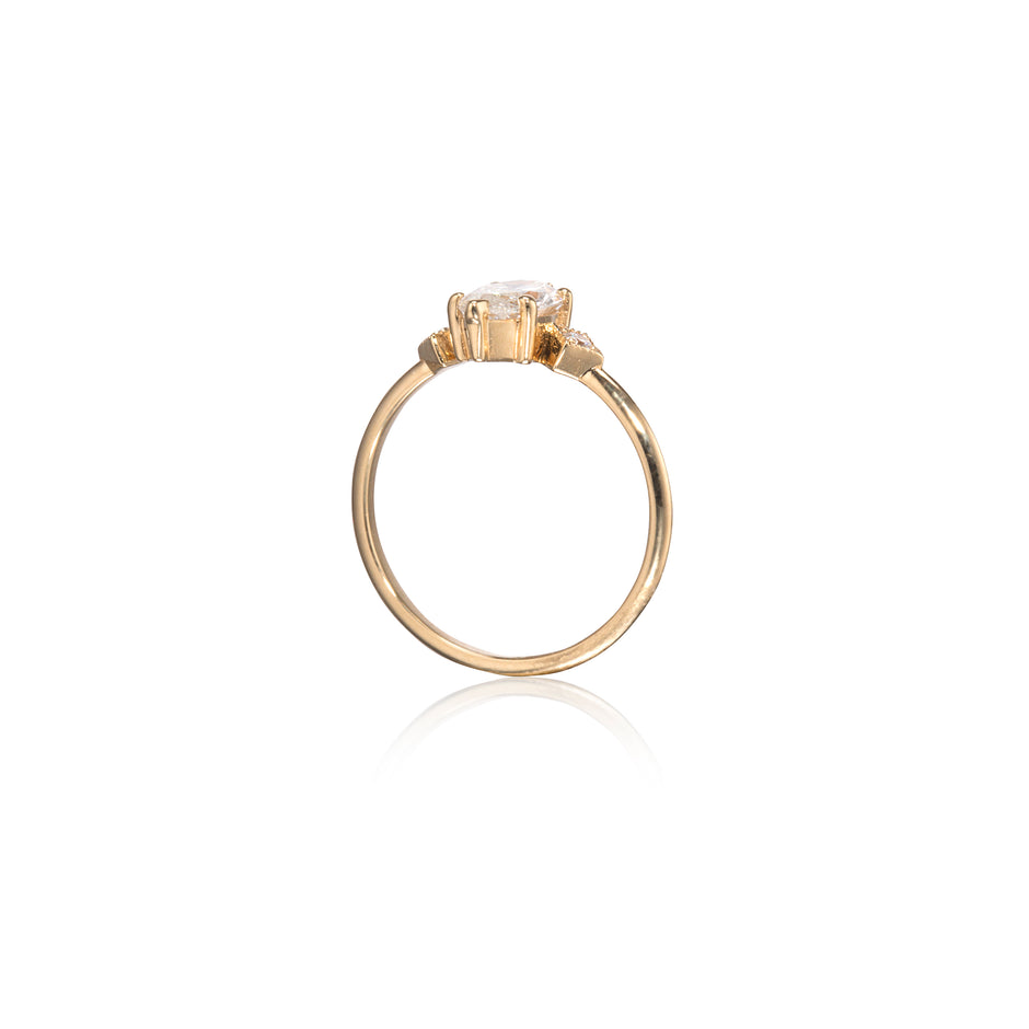 A yellow gold ring with a single round-cut clear gemstone in a prong setting, shown on a clean white background with a soft reflection below.