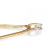 Close-up of a gold snake chain necklace with a clear round-cut gemstone in a silver setting, on a white reflective surface.