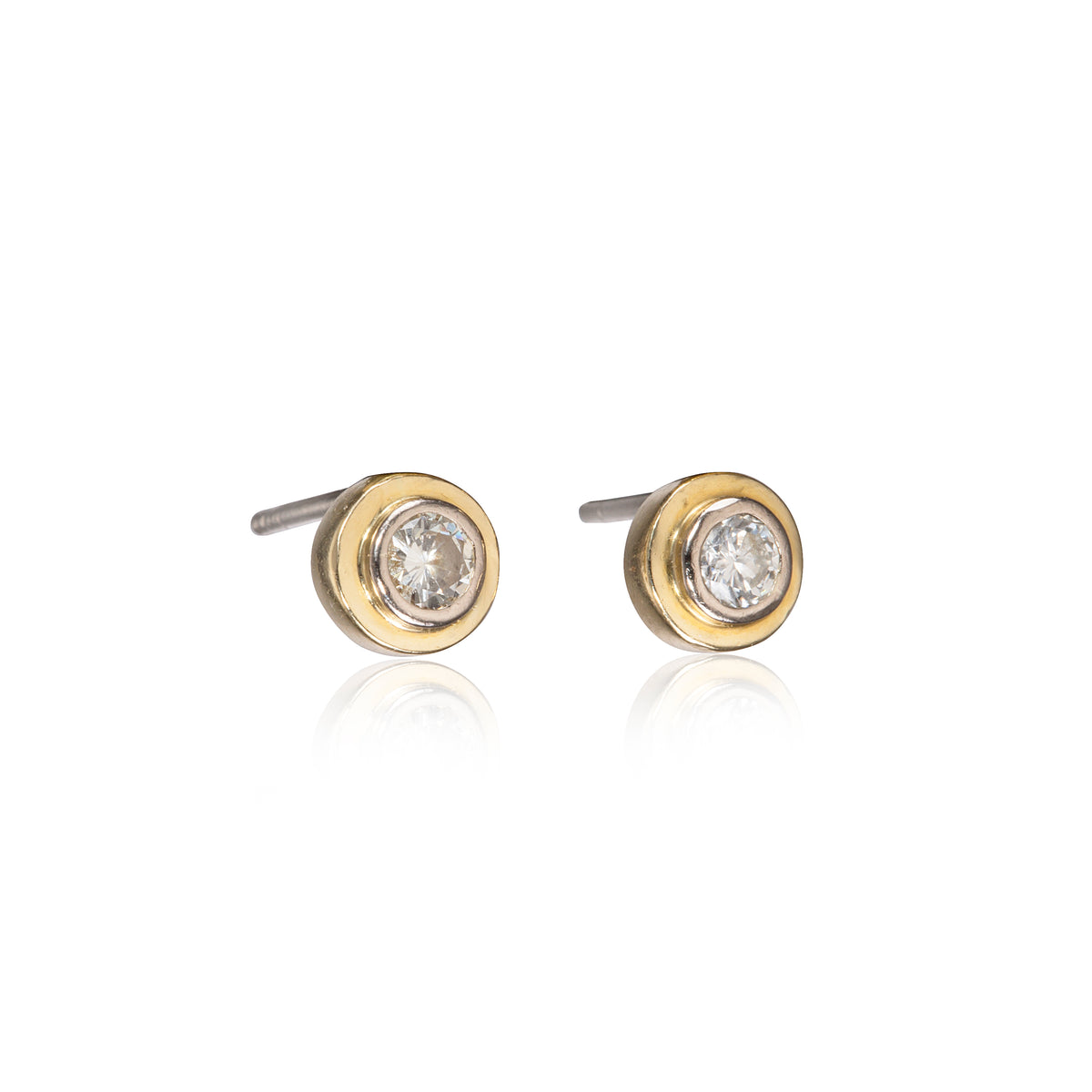 A pair of gold stud earrings with a clear round-cut gemstone in a bezel setting, shown on a white background with a soft reflection below.