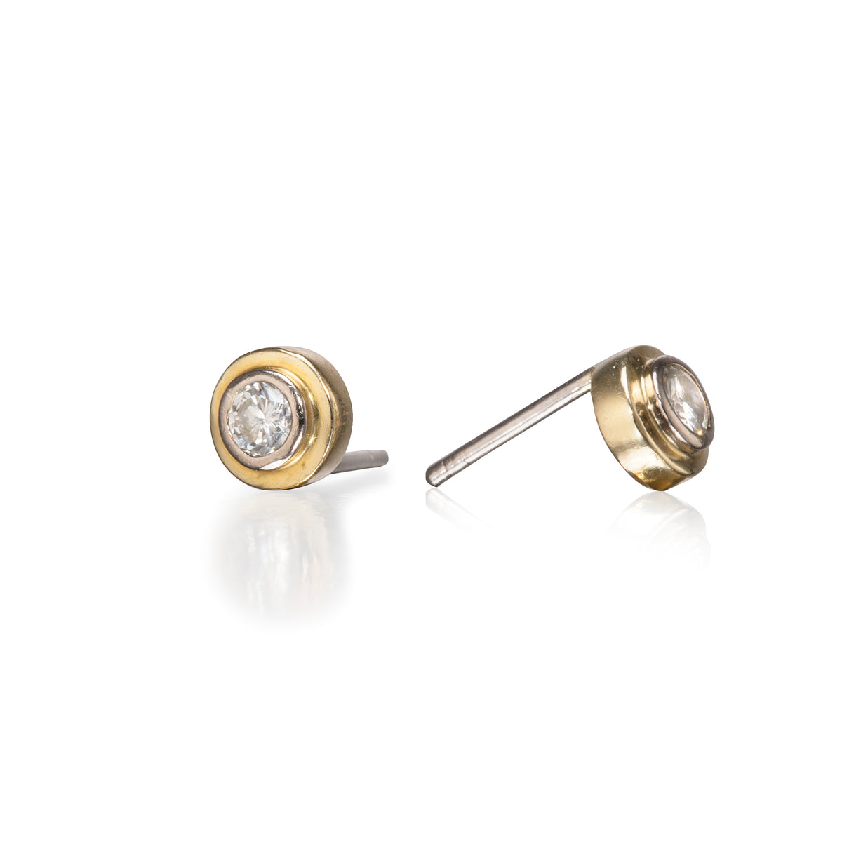 A pair of round gold stud earrings with clear gemstones, shown from two angles on a reflective white background.