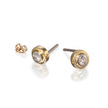 A pair of gold stud earrings with clear round-cut gemstones, shown on a white reflective background. One earring is shown from the side, displaying the gold post and backing, while the other is shown from the front and side.