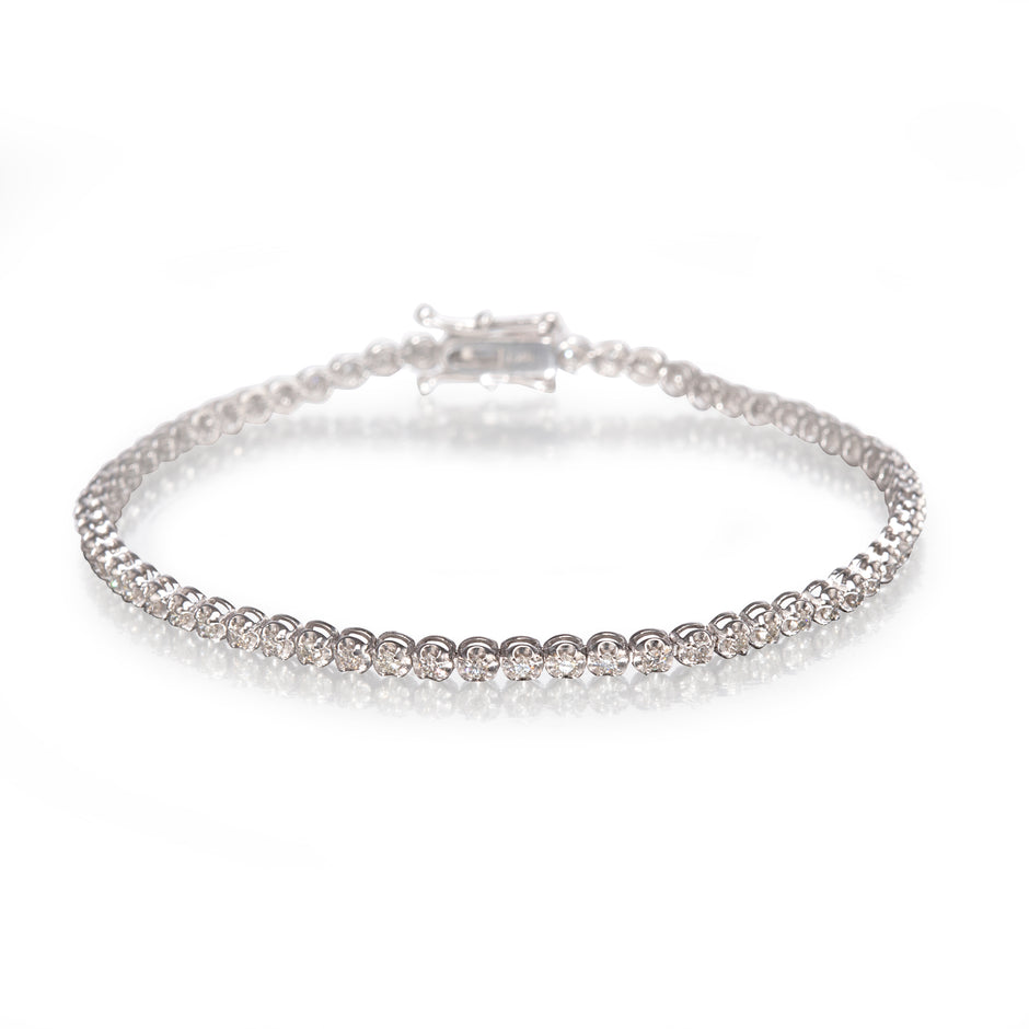 A white gold tennis bracelet with a continuous row of clear round-cut stones, displayed on a clean white reflective surface.