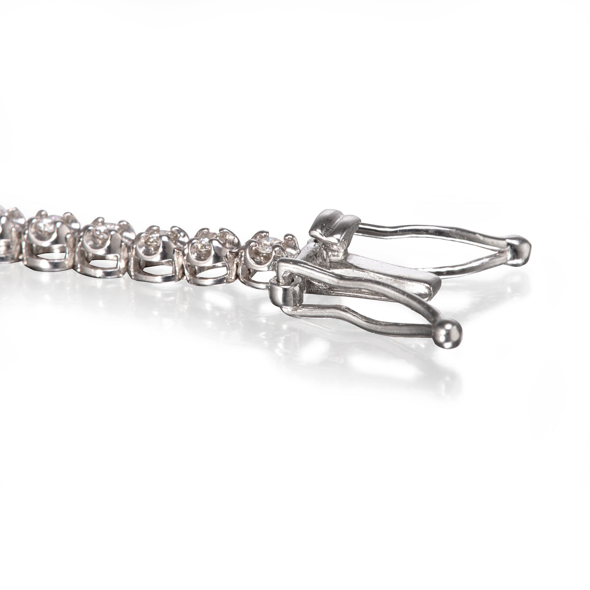 Close-up of a white gold tennis bracelet showing the clasp and part of the chain on a white reflective surface.