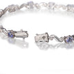 A white gold tennis bracelet with round blue tanzanite stones and clear accent stones, shown in a close-up on a reflective white surface.