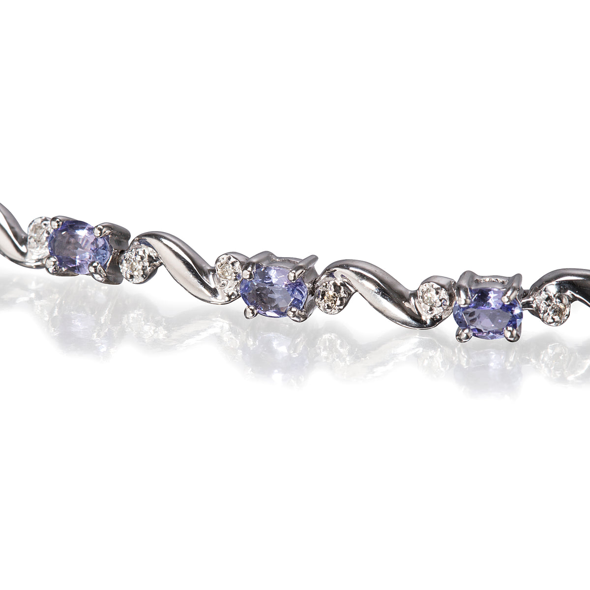 A close-up of a white gold tennis bracelet featuring oval tanzanite and round clear accent stones, set against a white background with a soft reflection.