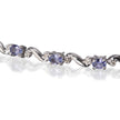 A close-up of a white gold tennis bracelet featuring oval tanzanite and round clear accent stones, set against a white background with a soft reflection.
