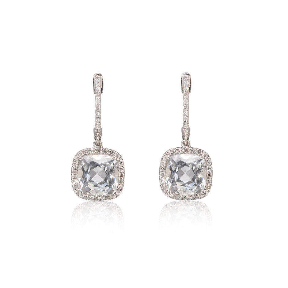 A pair of white gold drop earrings featuring cushion-cut clear gemstones surrounded by small pavé-set stones, shown on a white background with a soft reflection below.