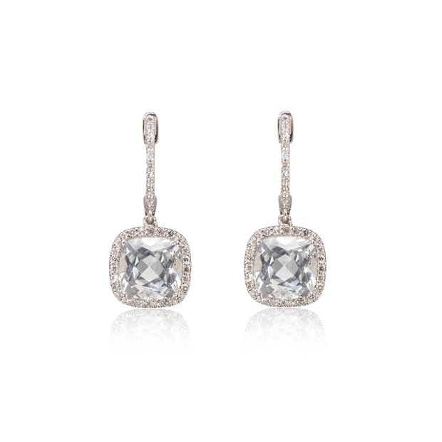 A pair of white gold drop earrings featuring cushion-cut clear gemstones surrounded by small pavé-set stones, shown on a white background with a soft reflection below.
