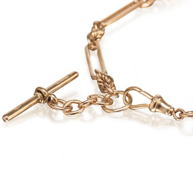 A close-up of a gold-toned chain bracelet with a toggle clasp and decorative links on a white background.