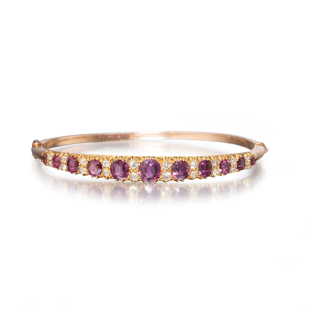 A rose gold bangle bracelet featuring a row of oval purple amethyst gemstones and small clear accent stones, shown on a clean white background with a soft reflection.