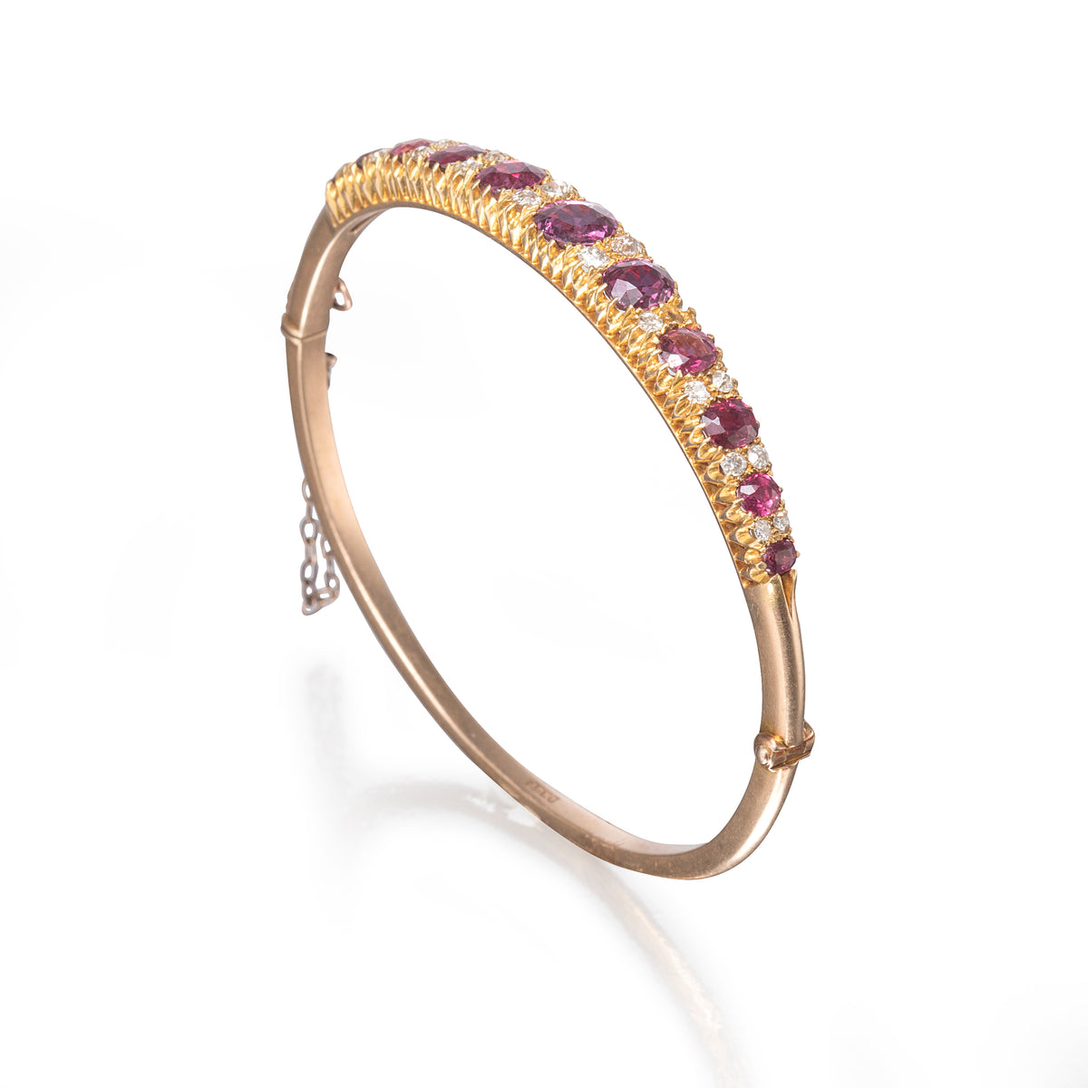 A gold hinged bangle bracelet featuring a row of oval pinkish-red gemstones and small clear stones, shown on a clean white background.