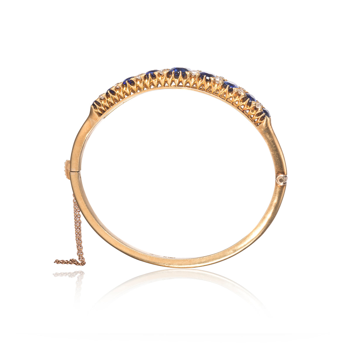 A gold hinged bangle bracelet,Antique Victorian Sapphire and Diamond Bangle, shown on a white background with a reflection.