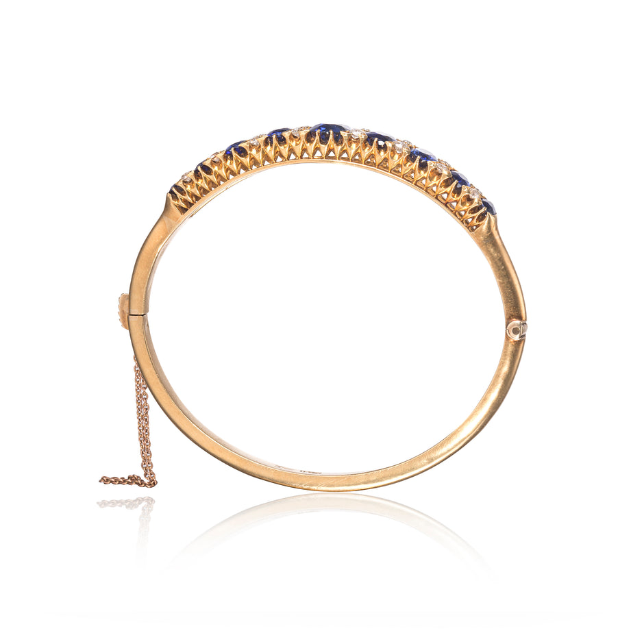 A gold hinged bangle bracelet,Antique Victorian Sapphire and Diamond Bangle, shown on a white background with a reflection.