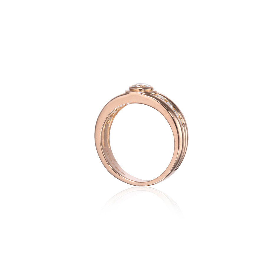 A rose gold ring with a small clear gemstone in a bezel setting, shown on a clean white background with a soft reflection below.