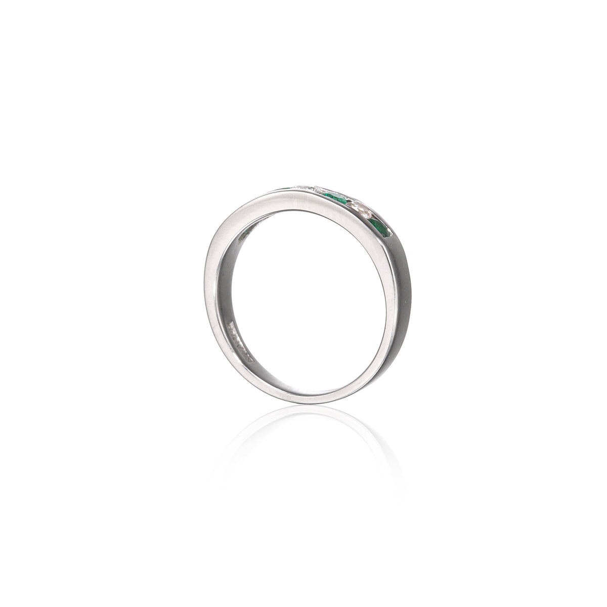 A white gold band ring featuring a row of small green gemstones on the front, displayed on a clean white background with a soft reflection below.