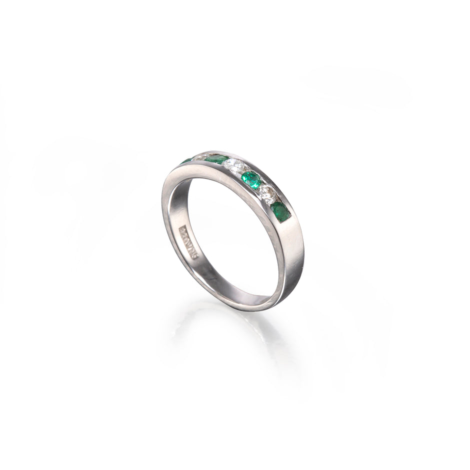 A white gold band ring featuring a row of green emerald-cut gemstones, photographed on a clean white background with a soft reflection.