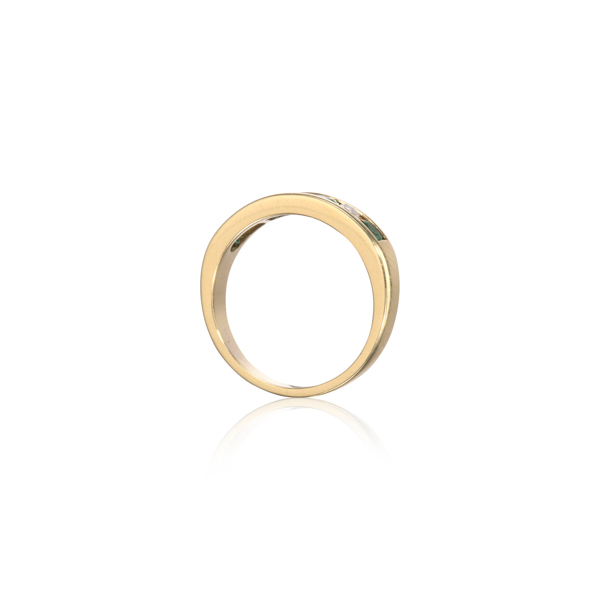 A polished yellow gold band ring with a small, clear, round-cut gemstone set on the upper right side, shown against a clean white background with a soft reflection below.