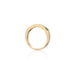 A polished yellow gold band ring with a small, clear, round-cut gemstone set on the upper right side, shown against a clean white background with a soft reflection below.