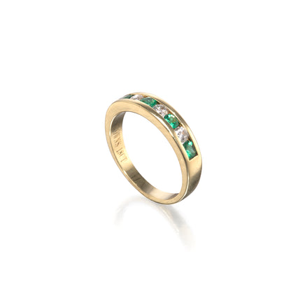 A yellow gold eternity ring featuring a channel-set row of green emerald-cut diamonds and clear round-cut diamonds, shown on a clean white background with a soft reflection.