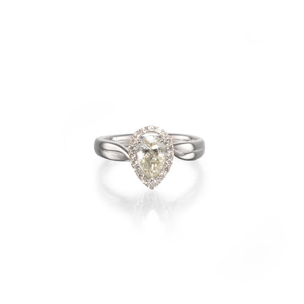 A pear-shaped diamond ring with a halo setting and a polished white gold band, centered on a clean white background with a soft reflection below.