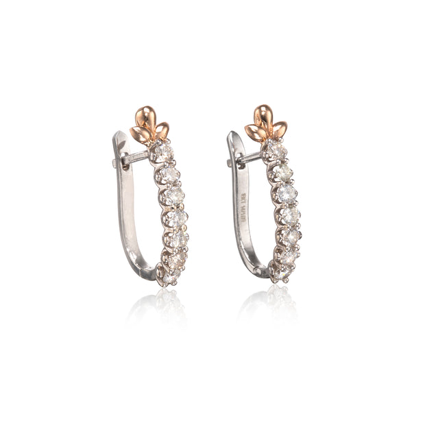 A pair of white gold hoop earrings with a vertical row of clear round-cut stones and a rose gold floral accent at the top, shown on a white background with a soft reflection.