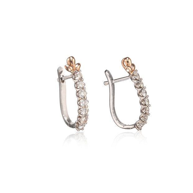A pair of white gold hoop earrings with a row of clear round-cut stones and a rose gold butterfly accent at the top, displayed on a clean white background with a soft reflection.