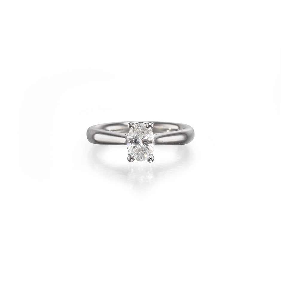An oval-cut diamond solitaire ring set on a polished platinum band, centered against a clean white background with a soft reflection below.