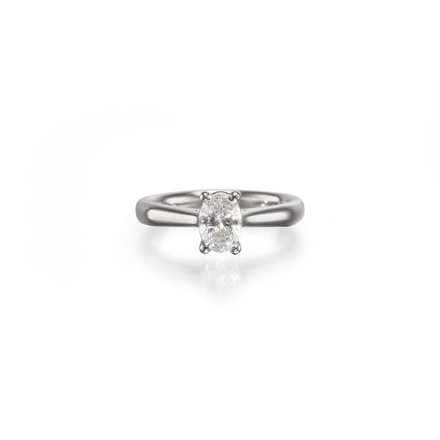 An oval-cut diamond solitaire ring set on a polished platinum band, centered against a clean white background with a soft reflection below.