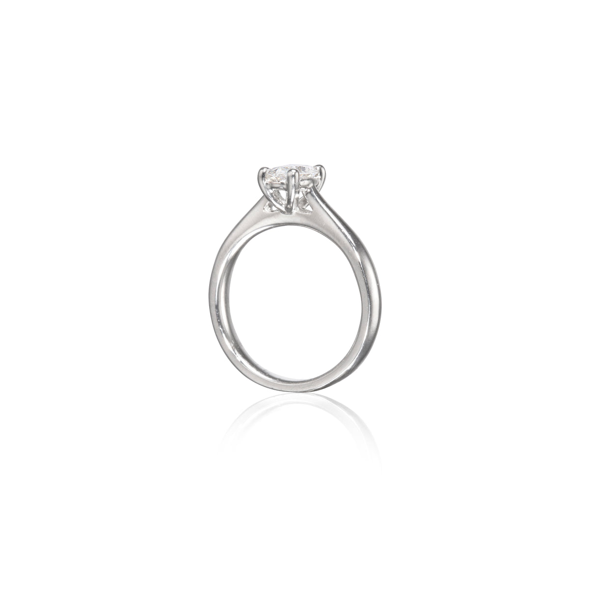 A platinum solitaire engagement ring with a round brilliant-cut diamond set in a four-prong setting, shown on a clean white background with a soft reflection below.