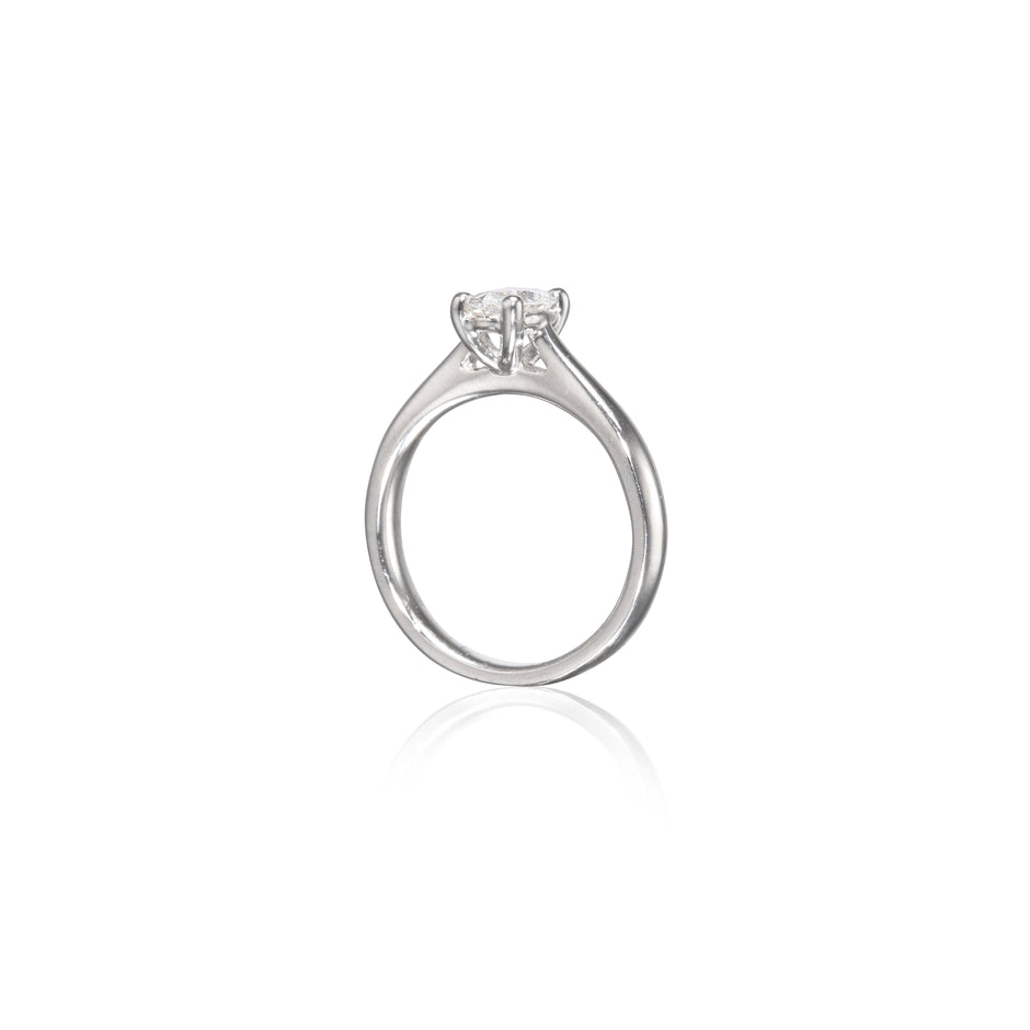 A platinum solitaire engagement ring with a round brilliant-cut diamond set in a four-prong setting, shown on a clean white background with a soft reflection below.