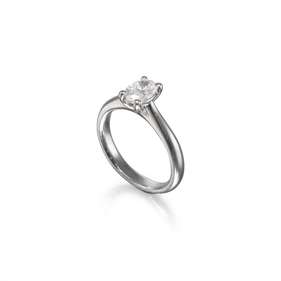 A platinum solitaire engagement ring with a round brilliant-cut diamond set in a four-prong setting, shown on a clean white background with a soft reflection.