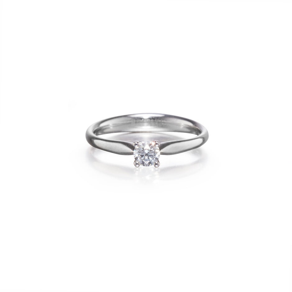 A platinum solitaire engagement ring with a clear round-cut gemstone, shown on a clean white background with a soft reflection.