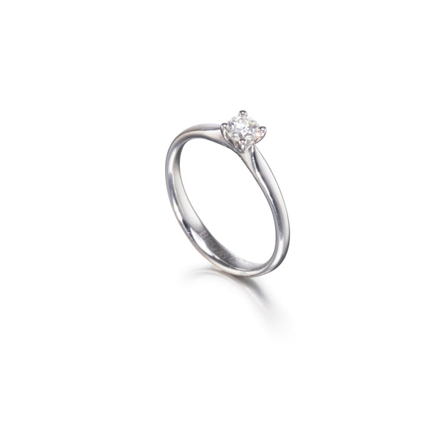 A platinum solitaire engagement ring with a round-cut diamond set in a four-prong setting, shown on a clean white background with a soft reflection.