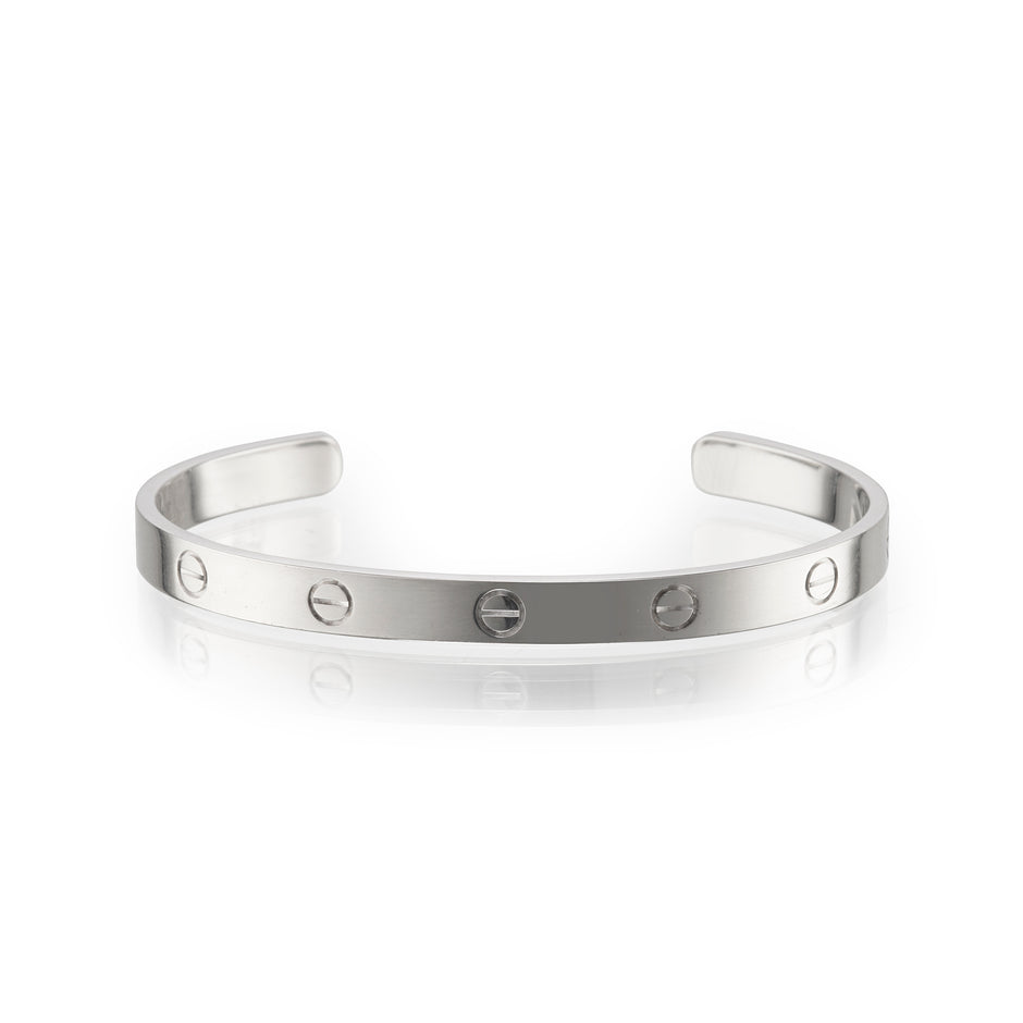 A white gold metal cuff bracelet with evenly spaced screw details, displayed on a clean white background with a soft reflection.