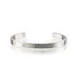 A white gold metal cuff bracelet with evenly spaced screw details, displayed on a clean white background with a soft reflection.
