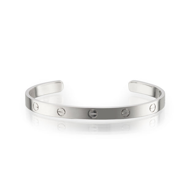 A white gold metal cuff bracelet with evenly spaced screw details, displayed on a clean white background with a soft reflection.