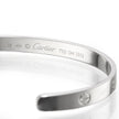 A close-up of a polished white gold Cartier bangle bracelet, showing the engraved brand name, 'Cartier', model number '750', and screw details on a reflective white surface.