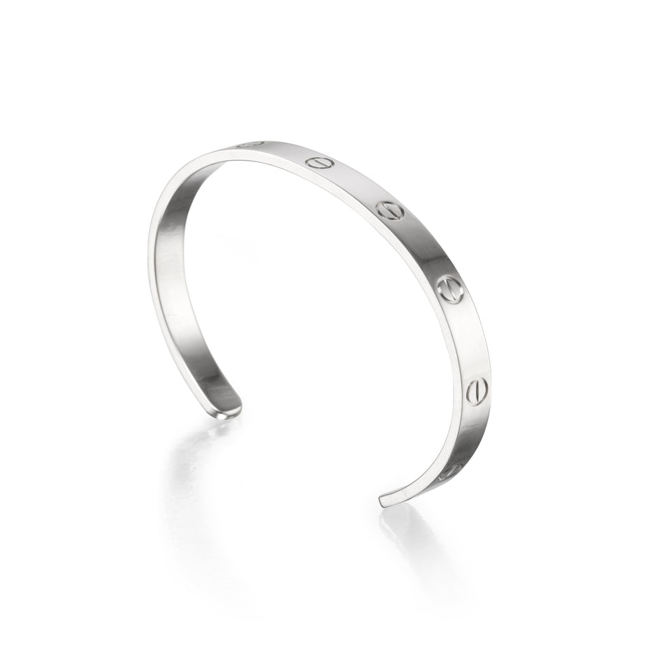 A white gold metal cuff bracelet with four evenly spaced screw-head details, photographed on a clean white background with a soft reflection.