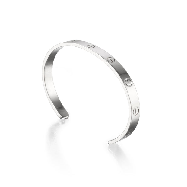 A white gold metal cuff bracelet with four evenly spaced screw-head details, photographed on a clean white background with a soft reflection.
