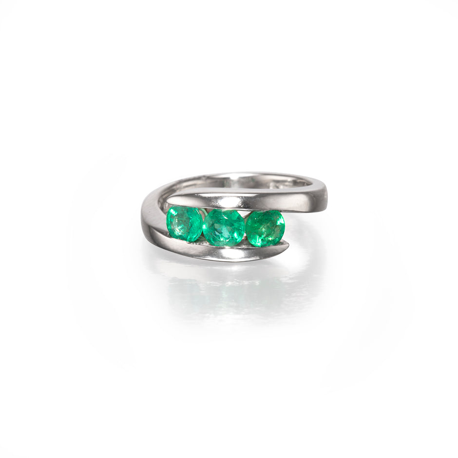 A Charles Greig Platinum ring featuring three round-cut green emerald-cut gemstones in a row, set against a clean white background with a soft reflection.