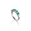 A white gold ring featuring a row of oval-cut green emeralds and small clear accent stones, shown on a clean white background with a soft reflection.