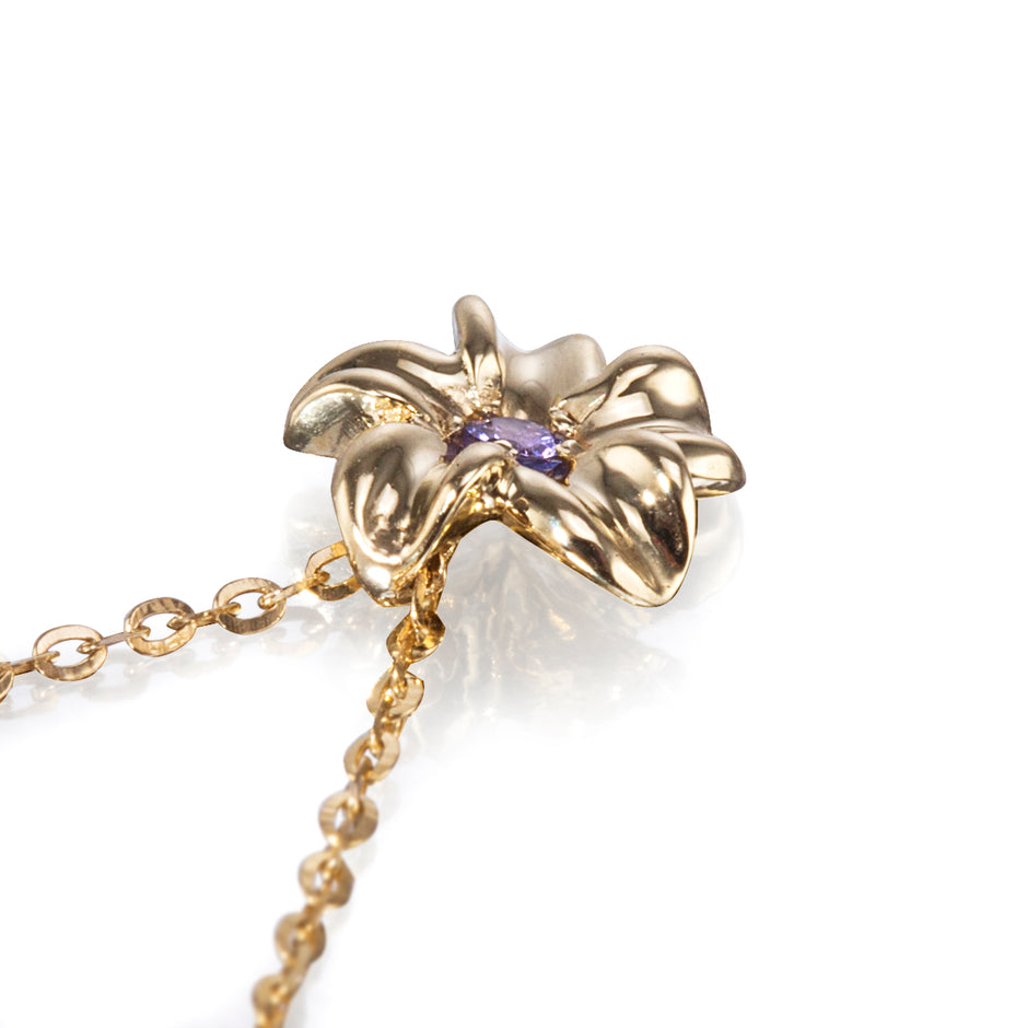 A gold flower-shaped pendant necklace with a small purple gemstone in the center, shown on a clean white background.