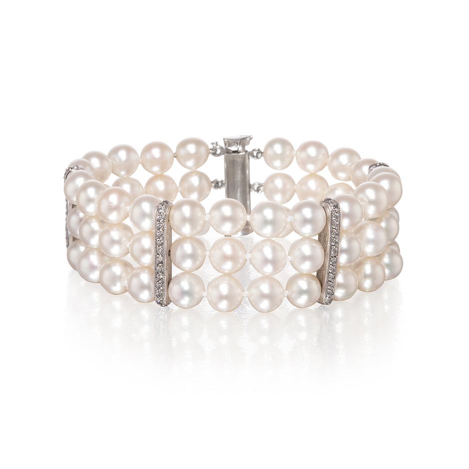 A multi-row pearl bracelet with white gold metal links and clear rhinestone accents, displayed on a clean white background with a soft reflection.