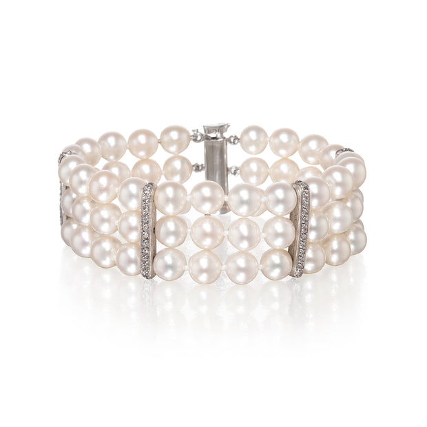 A multi-row pearl bracelet with white gold metal links and clear rhinestone accents, displayed on a clean white background with a soft reflection.