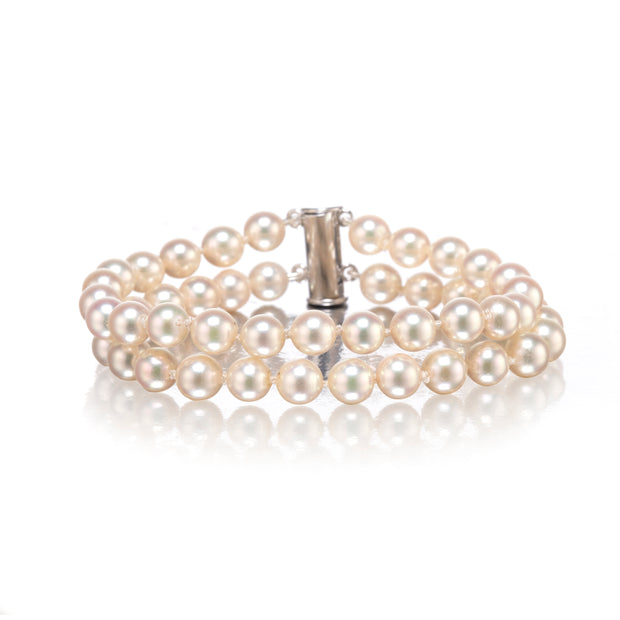A double-strand pearl bracelet with a polished silver clasp, displayed on a clean white background with a soft reflection.