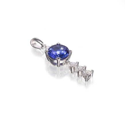 A platinum pendant featuring a round blue tanzanite center stone and three marquise-cut clear stones in a drop design, set on a white background with a soft reflection.