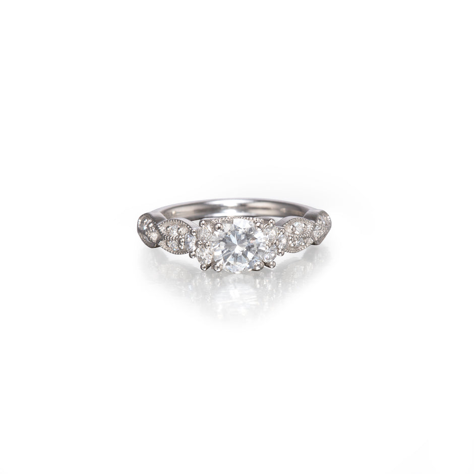 A platinum diamond ring with a central round-cut diamond surrounded by smaller diamonds along the band, set against a plain white background with a soft reflection below.