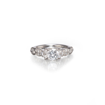 A platinum diamond ring with a central round-cut diamond surrounded by smaller diamonds along the band, set against a plain white background with a soft reflection below.